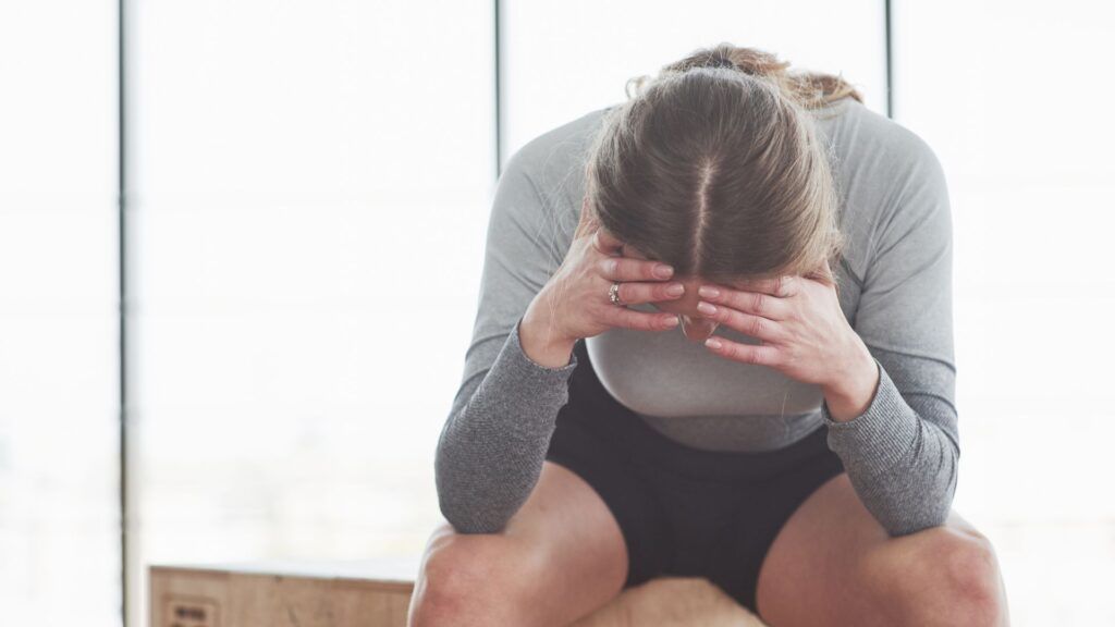Mujer sentada con la cabeza entre las manos mostrando signos de estr&eacute;s, malestar emocional y cansancio. La fotograf&iacute;a ilustra c&oacute;mo las adicciones pueden afectar al bienestar psicol&oacute;gico, favoreciendo la aparici&oacute;n de ansiedad, tristeza y dificultades para afrontar el d&iacute;a a d&iacute;a.
